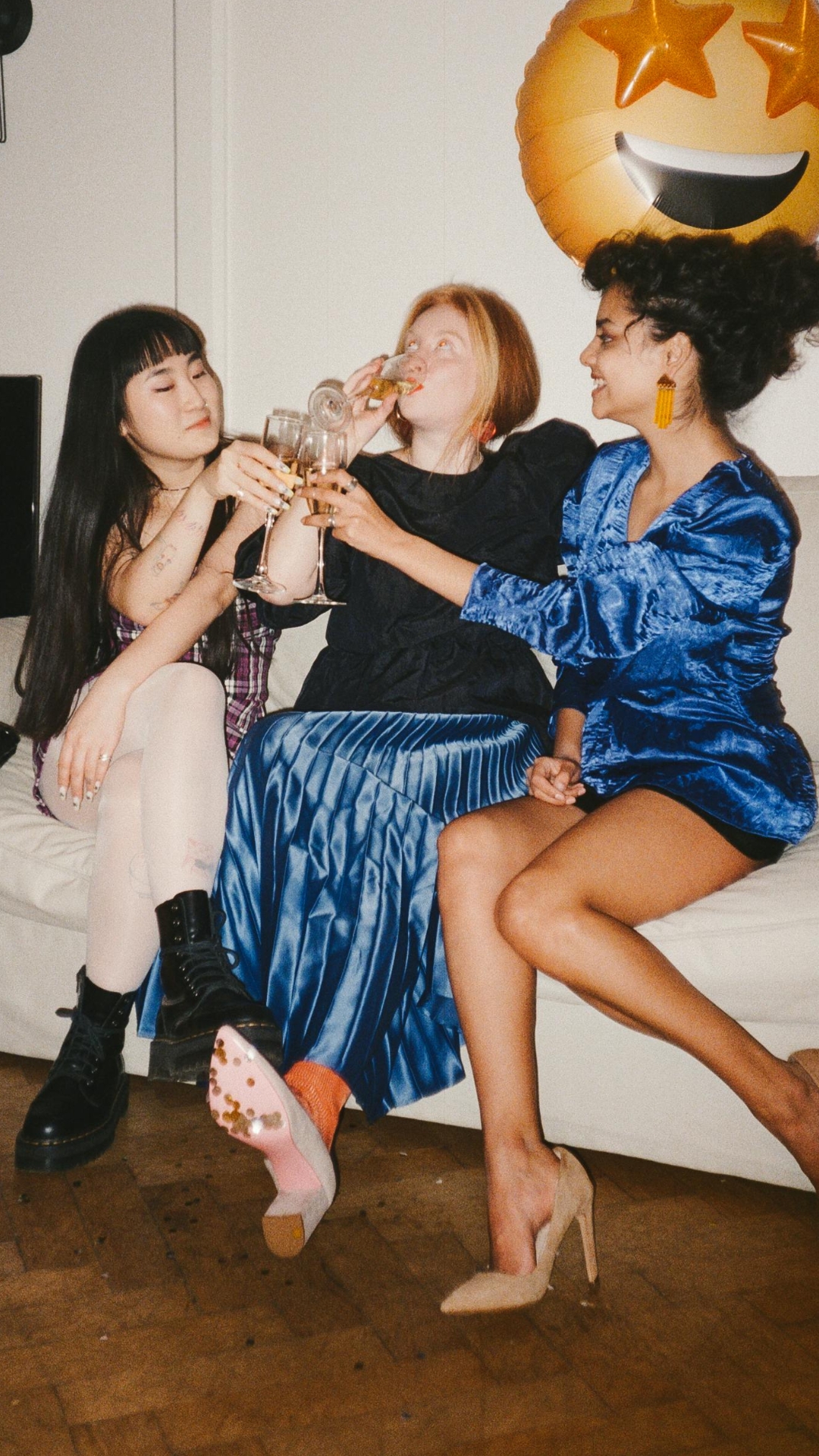 three women sit on a couch while drinking at a party [article: Best never have i ever questions to ask)