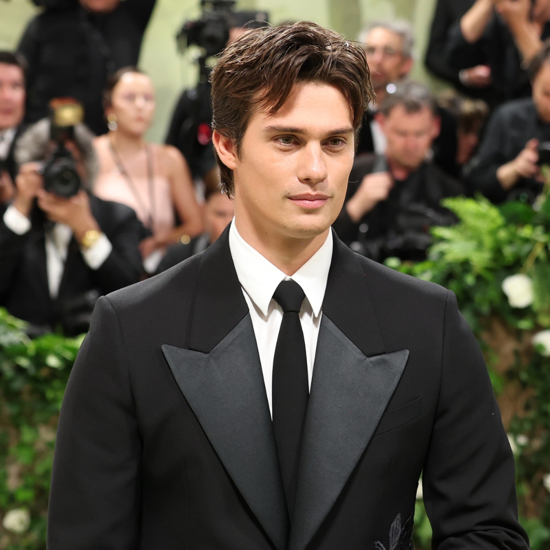 A headshot of nicholas galitzine at the 2024 met gala. He wears a black suit jacket, white dress shirt and a black tie