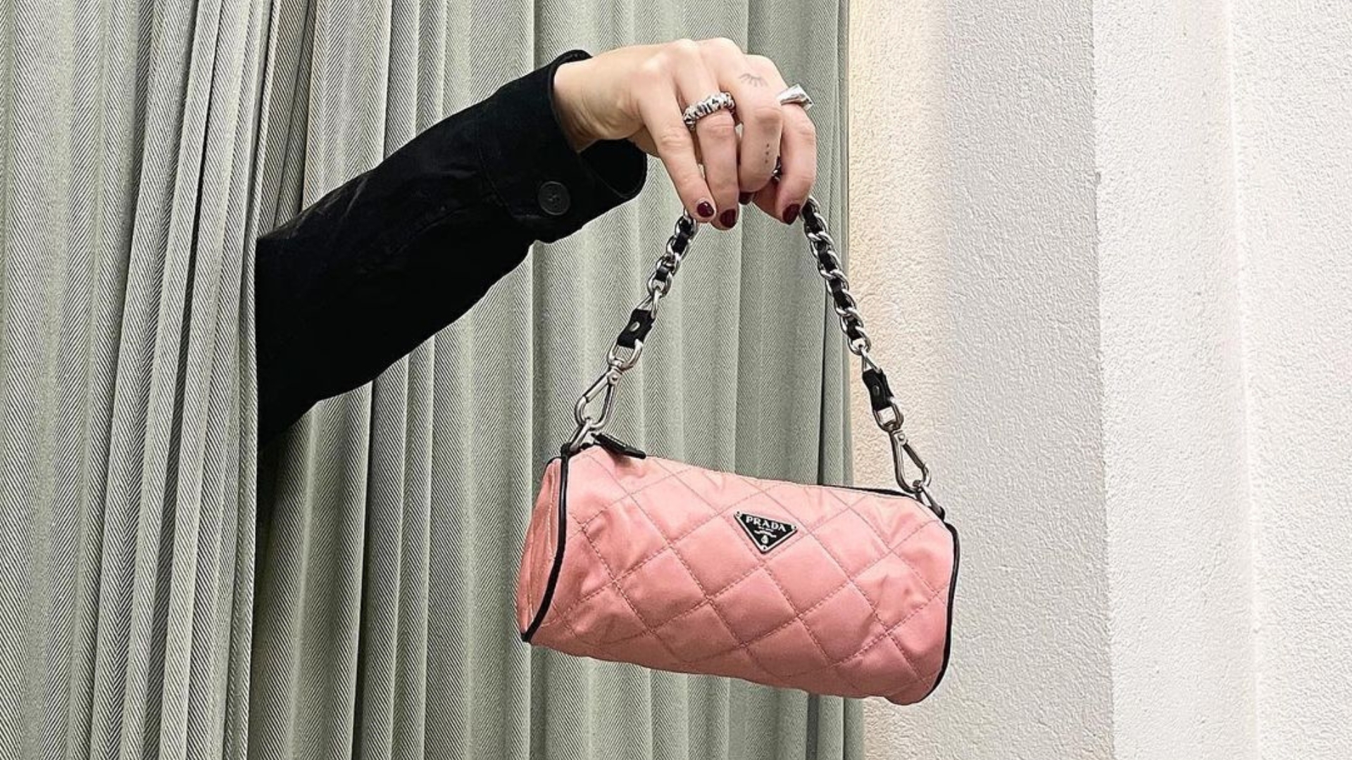 at a vintage fashion store, an employ holds a pink handbag out from teal curtains