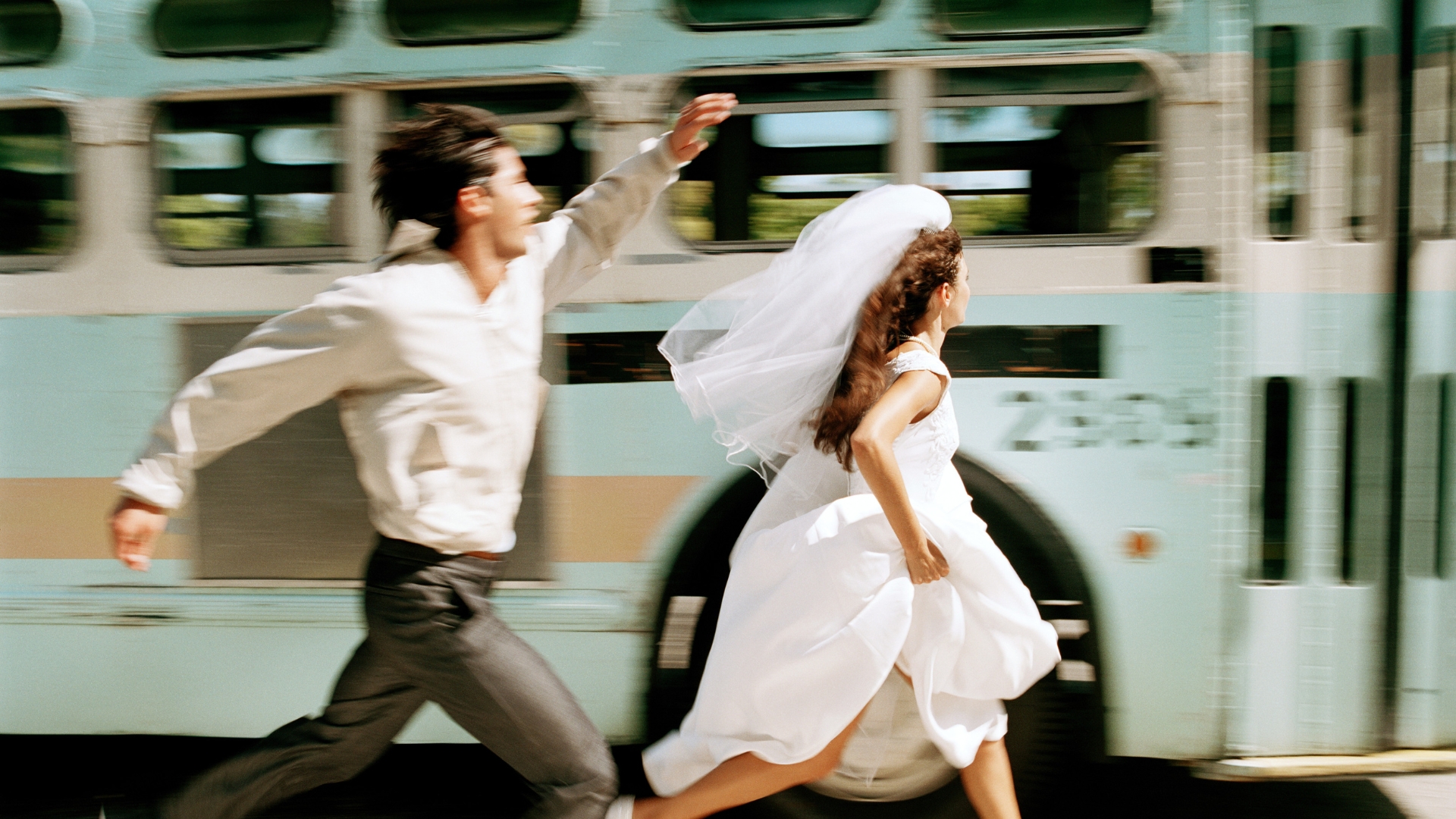 couple running alongside a blue bus (story: taking your partner's name pros cons)