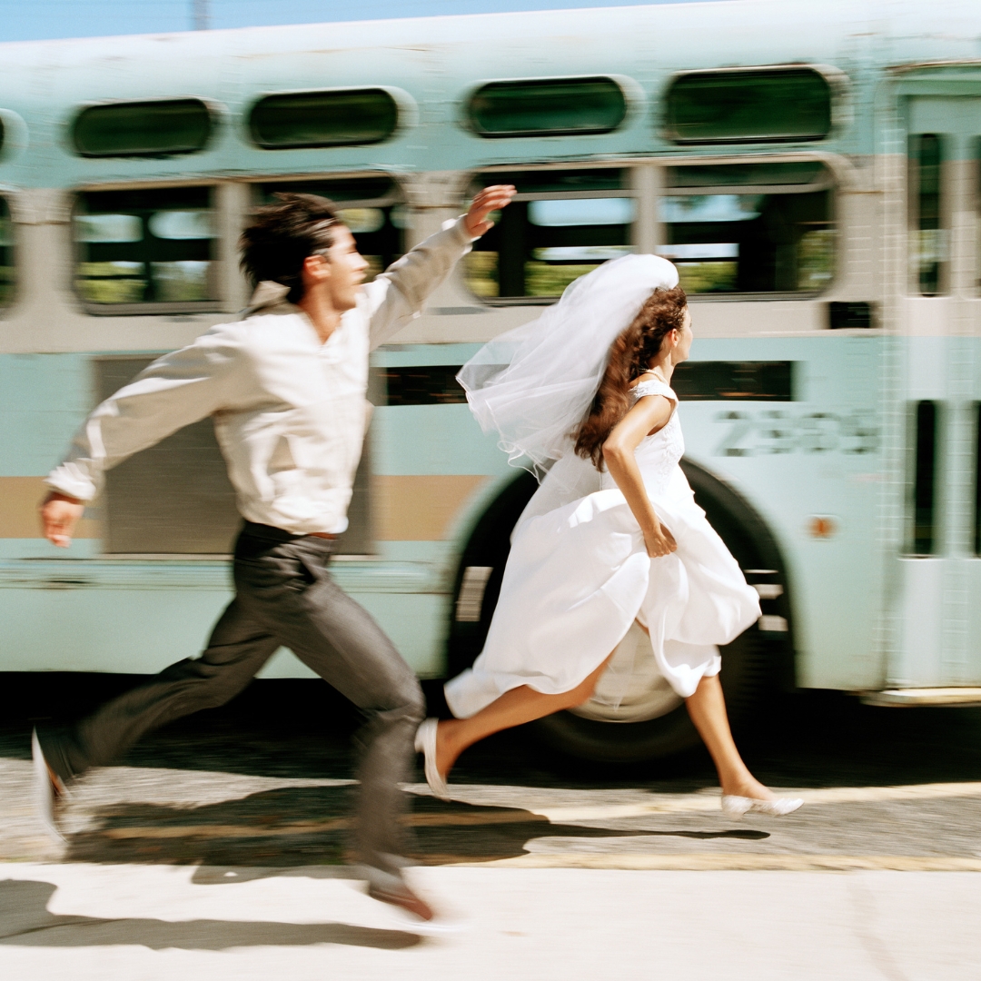 couple running alongside a blue bus (story: taking your partner's name pros cons)